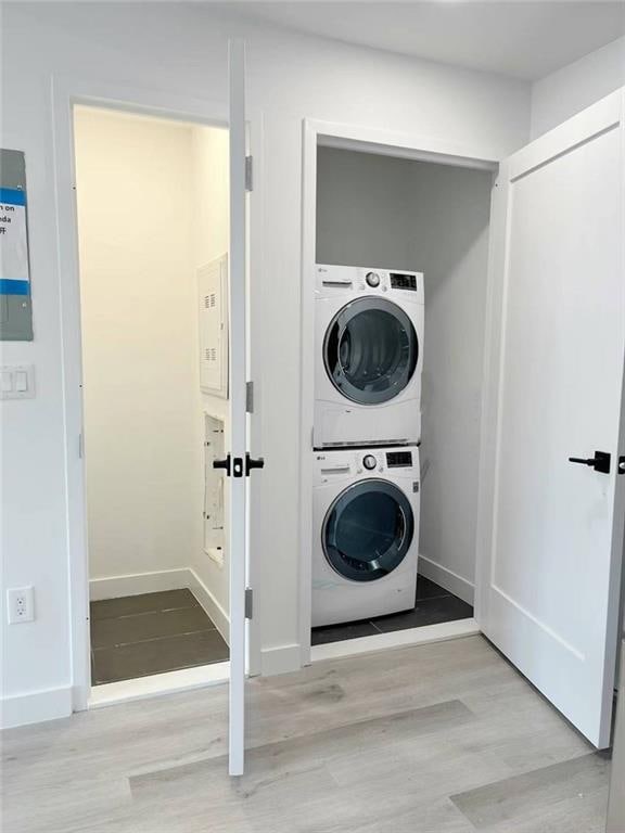 laundry area with stacked washer and dryer, wood finished floors, laundry area, and baseboards