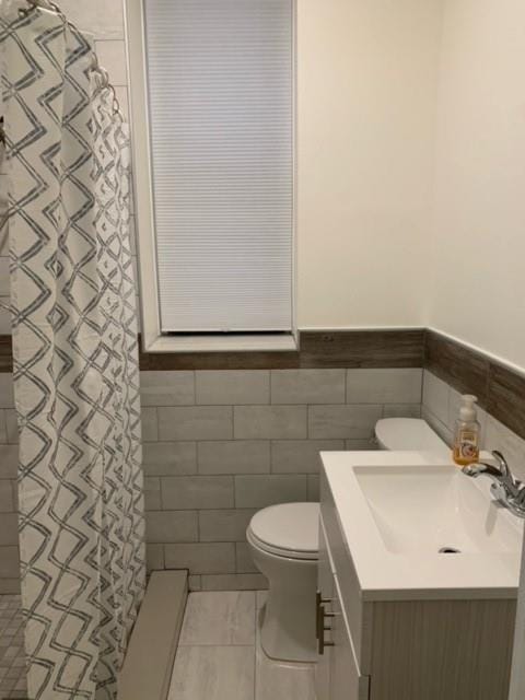 bathroom with tile walls, toilet, vanity, and tile patterned floors