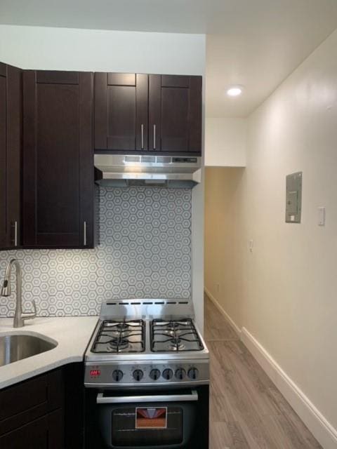 kitchen with double oven range, light hardwood / wood-style floors, wall chimney exhaust hood, dark brown cabinetry, and sink