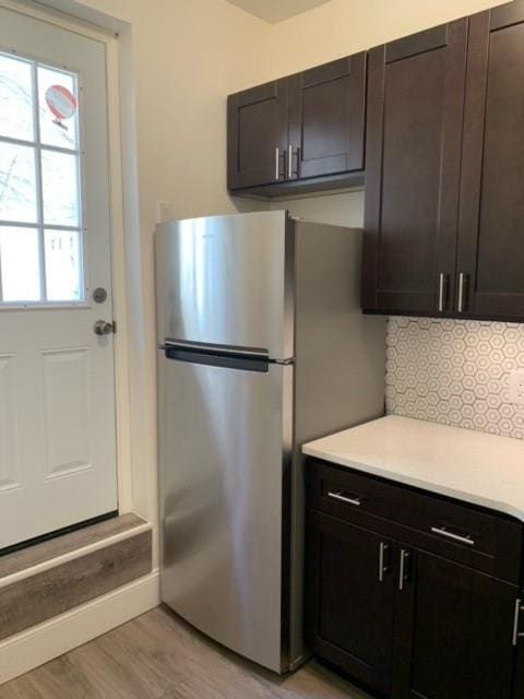 kitchen featuring decorative backsplash, light hardwood / wood-style flooring, dark brown cabinetry, and stainless steel refrigerator