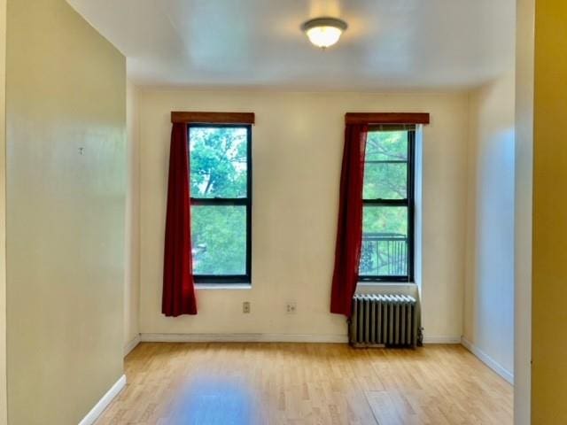 empty room with a wealth of natural light, light hardwood / wood-style flooring, and radiator