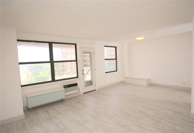 empty room featuring a wall unit AC, radiator, light wood-type flooring, and a wealth of natural light