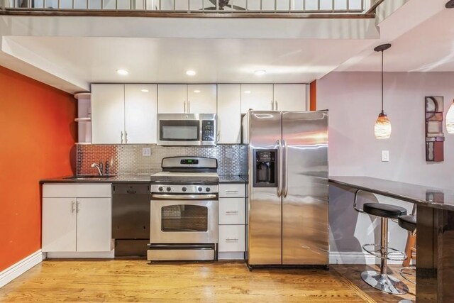 kitchen featuring white cabinetry, sink, hanging light fixtures, stainless steel appliances, and light hardwood / wood-style floors