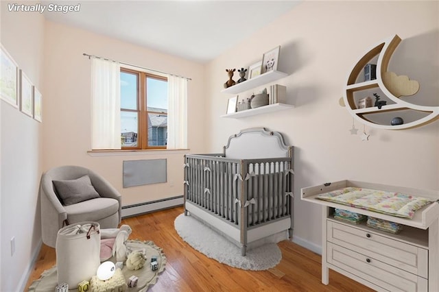 bedroom with a crib, wood finished floors, baseboards, and baseboard heating