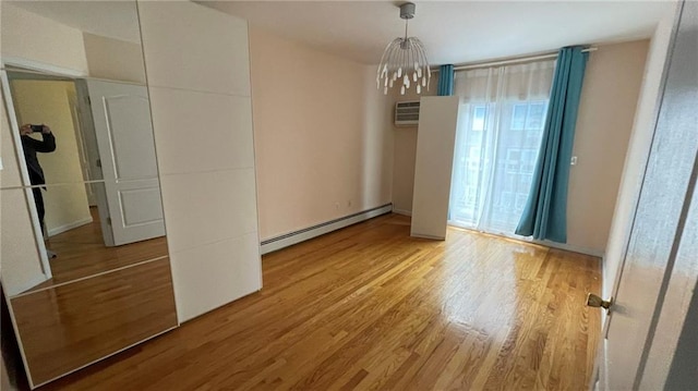 interior space with an inviting chandelier, a baseboard heating unit, and wood-type flooring