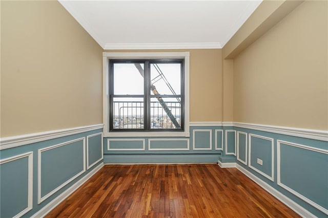 spare room with a wainscoted wall, ornamental molding, dark wood-style flooring, and a decorative wall