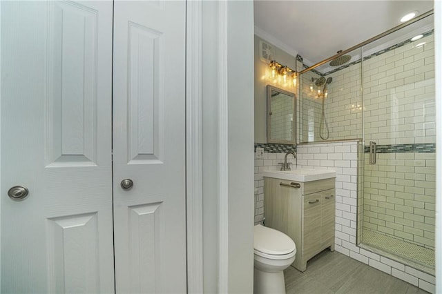 bathroom featuring a shower stall, crown molding, tile walls, toilet, and vanity