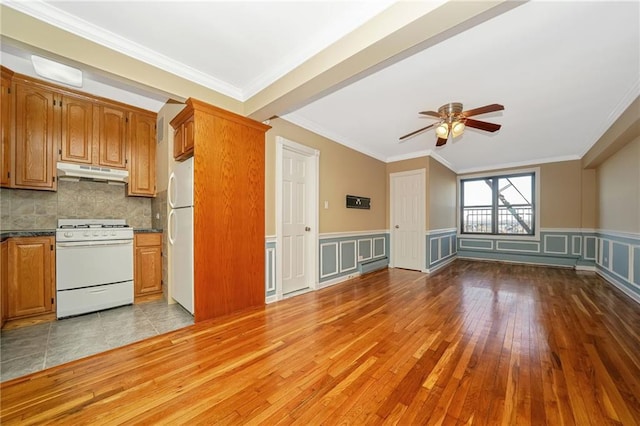 kitchen featuring tasteful backsplash, dark countertops, under cabinet range hood, brown cabinetry, and white appliances