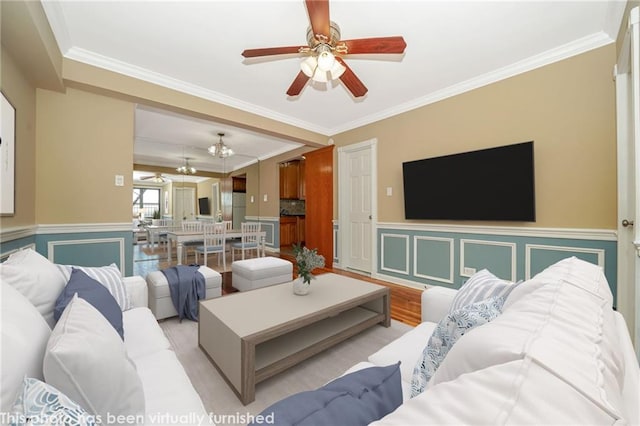 living area with a wainscoted wall, a ceiling fan, light wood-style floors, and ornamental molding