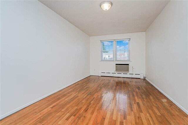 empty room featuring hardwood / wood-style flooring and a baseboard heating unit