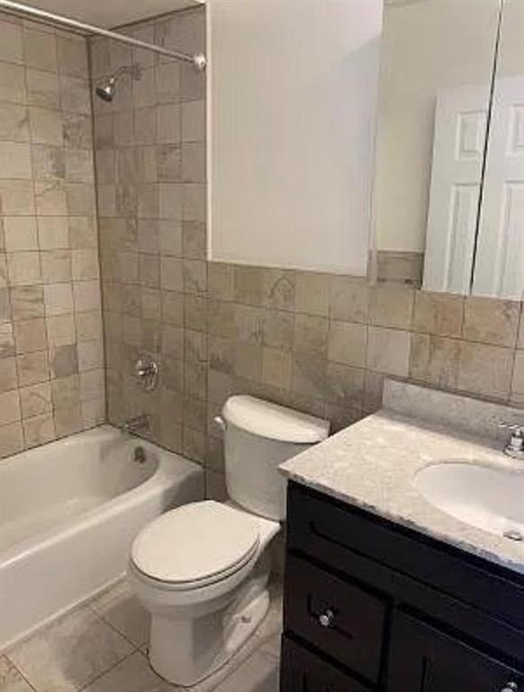 full bathroom featuring tiled shower / bath, tile walls, vanity, toilet, and tile patterned floors