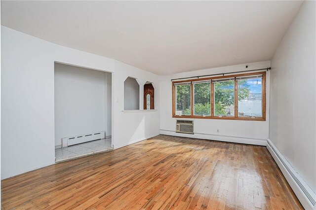 spare room featuring a baseboard heating unit, a wall mounted air conditioner, and hardwood / wood-style floors