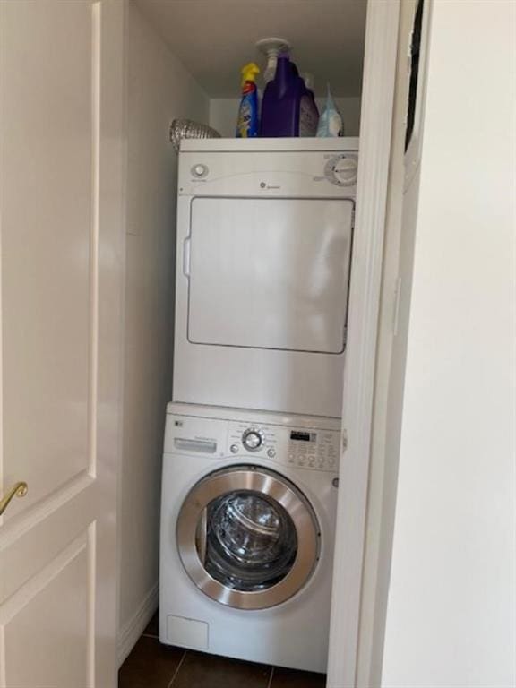 clothes washing area featuring stacked washer / drying machine and dark tile patterned flooring