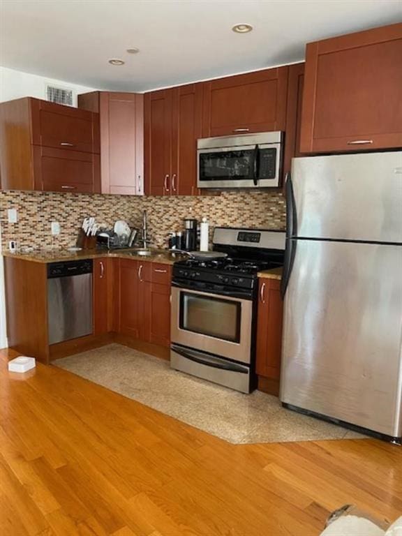 kitchen with tasteful backsplash, appliances with stainless steel finishes, sink, and light hardwood / wood-style floors