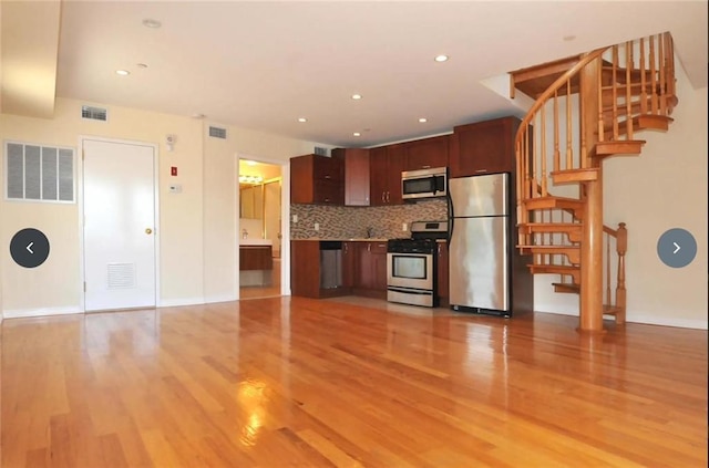 kitchen with appliances with stainless steel finishes, light hardwood / wood-style flooring, and backsplash