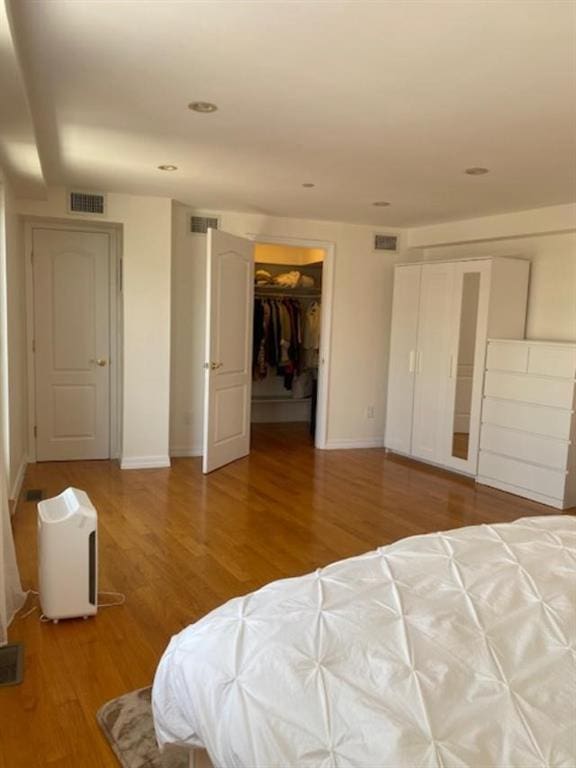 bedroom with a walk in closet and wood-type flooring