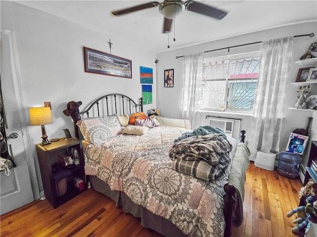 bedroom with a wall mounted AC, hardwood / wood-style flooring, and ceiling fan