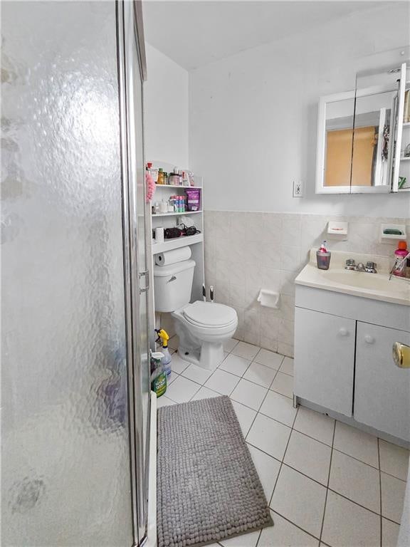 bathroom featuring toilet, an enclosed shower, tile walls, vanity, and tile patterned flooring