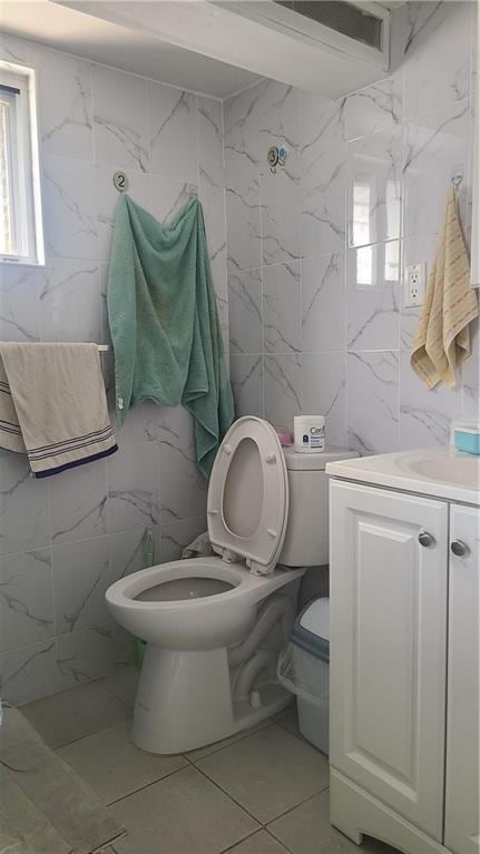 bathroom featuring plenty of natural light, vanity, toilet, and tile walls