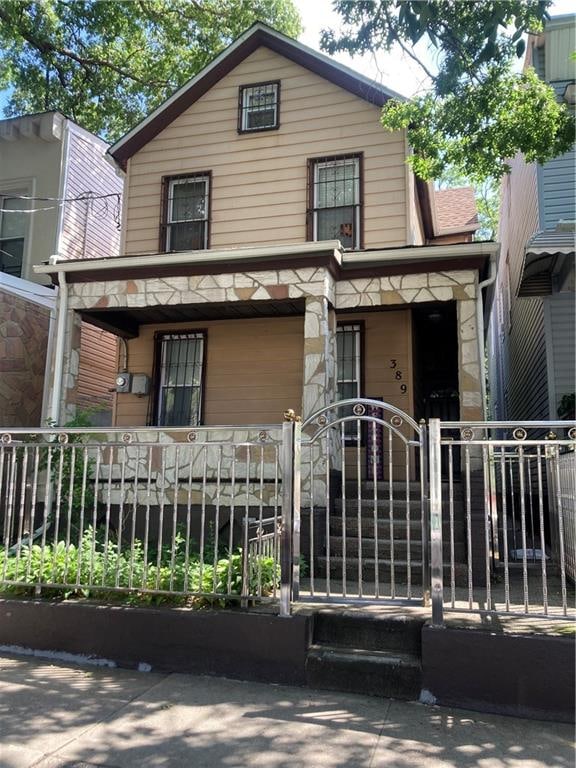 389 Warwick St, Brooklyn, NY 11207 - view of front of property with a gate, covered porch, a fenced front yard, and stone siding