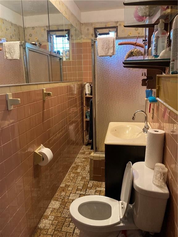 bathroom with vanity, a shower with shower door, tile walls, and toilet