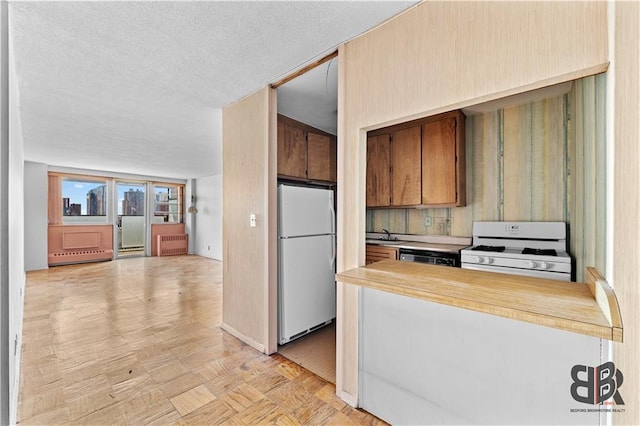 kitchen featuring white appliances, a textured ceiling, radiator, light parquet flooring, and a baseboard heating unit