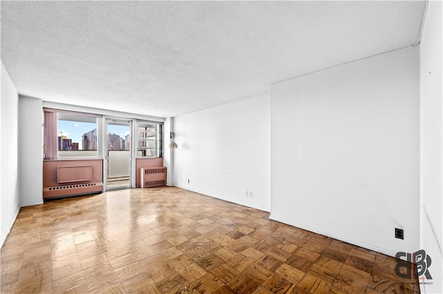 empty room featuring light parquet floors, radiator heating unit, a textured ceiling, and baseboard heating