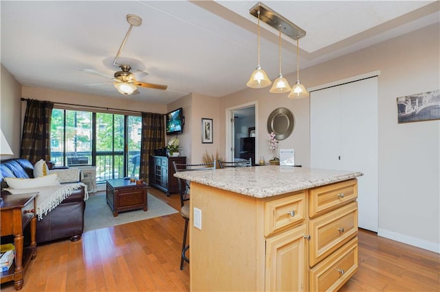 kitchen featuring a kitchen island, light brown cabinetry, light wood-type flooring, ceiling fan, and a breakfast bar