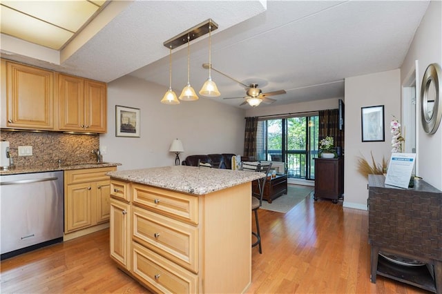 kitchen featuring pendant lighting, light brown cabinetry, dishwasher, a kitchen bar, and a kitchen island