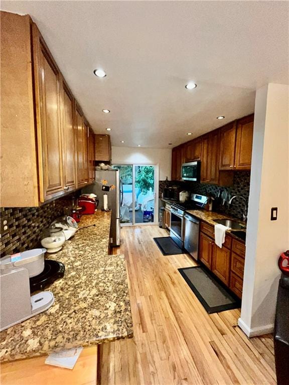 kitchen featuring light stone countertops, sink, stainless steel appliances, decorative backsplash, and light wood-type flooring