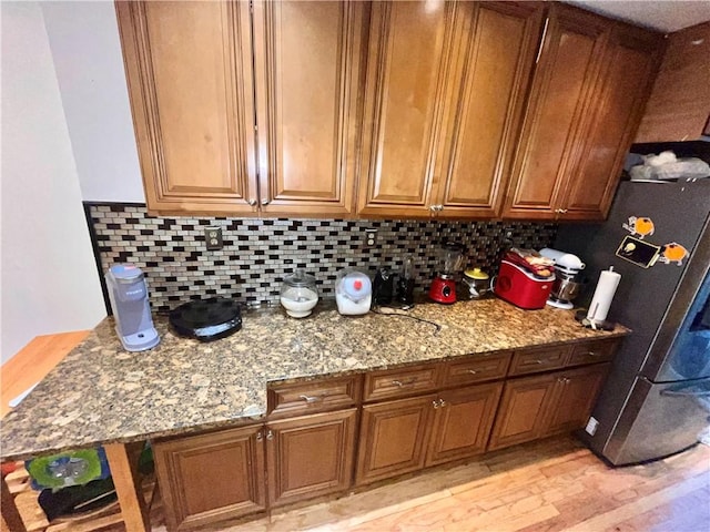 kitchen featuring backsplash, light hardwood / wood-style floors, stainless steel refrigerator, and light stone counters