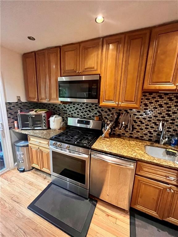 kitchen featuring sink, decorative backsplash, light stone countertops, light wood-type flooring, and stainless steel appliances