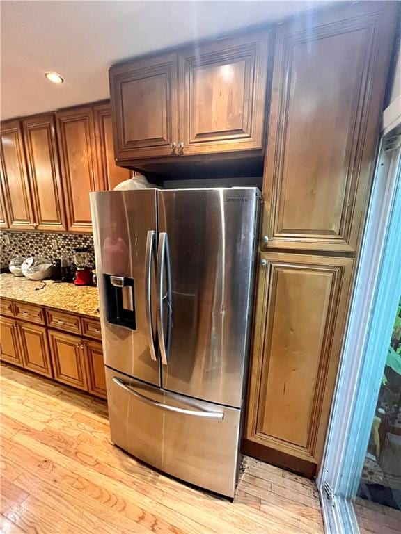 kitchen with light stone countertops, stainless steel fridge with ice dispenser, backsplash, and light hardwood / wood-style flooring