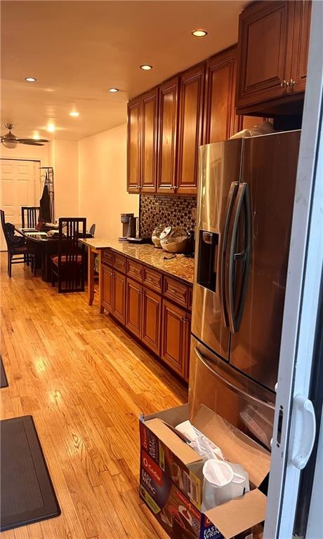 kitchen featuring light stone countertops, stainless steel fridge, backsplash, ceiling fan, and light hardwood / wood-style flooring