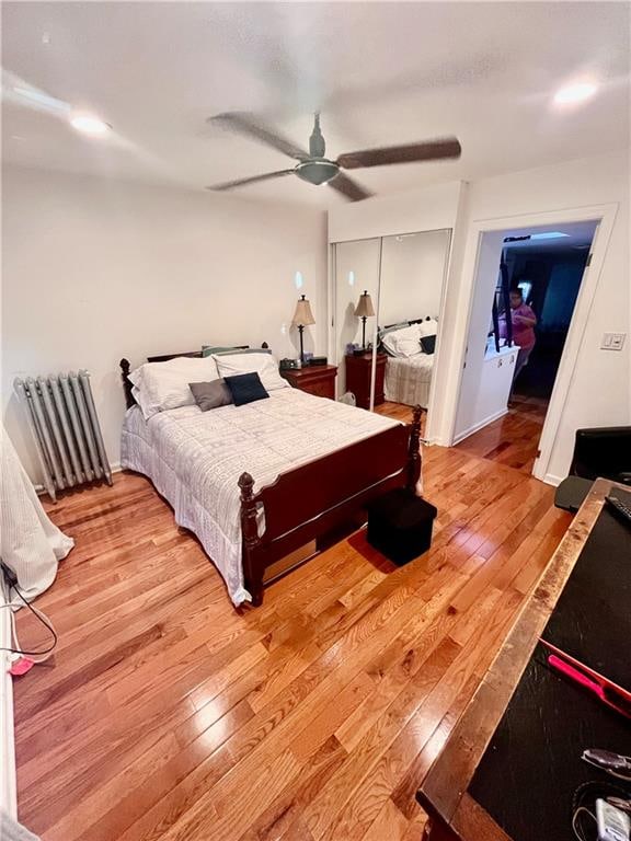 bedroom with hardwood / wood-style flooring, ceiling fan, radiator, and a closet