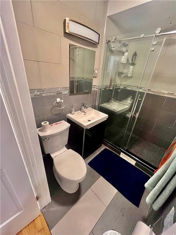 bathroom featuring vanity, toilet, tile walls, an enclosed shower, and wood-type flooring