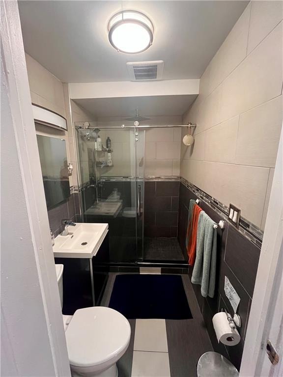 bathroom with tile patterned floors, toilet, a shower with door, vanity, and tile walls