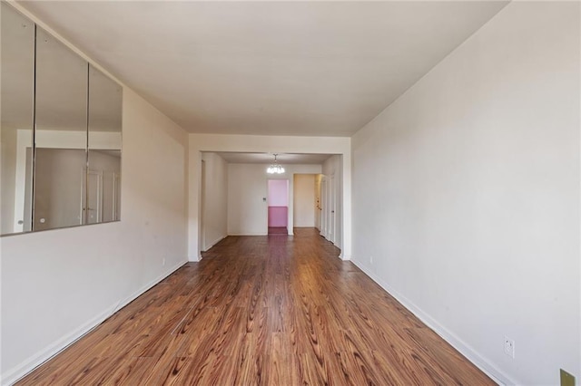 corridor featuring a notable chandelier, wood finished floors, and baseboards