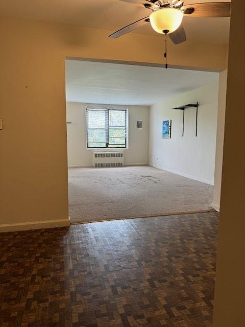 spare room featuring dark parquet flooring, radiator heating unit, and ceiling fan