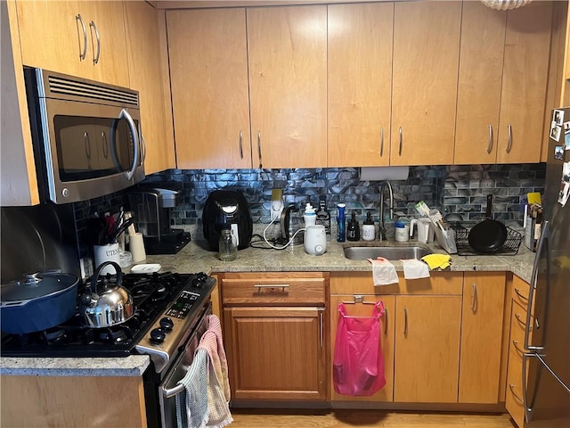 kitchen with light stone counters, appliances with stainless steel finishes, sink, and decorative backsplash