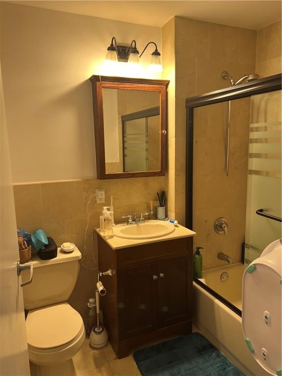 full bathroom with combined bath / shower with glass door, tile walls, tile patterned flooring, vanity, and toilet