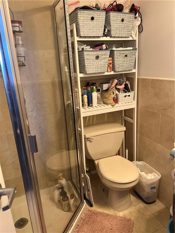 bathroom with tile patterned floors, toilet, a shower with shower door, and tile walls