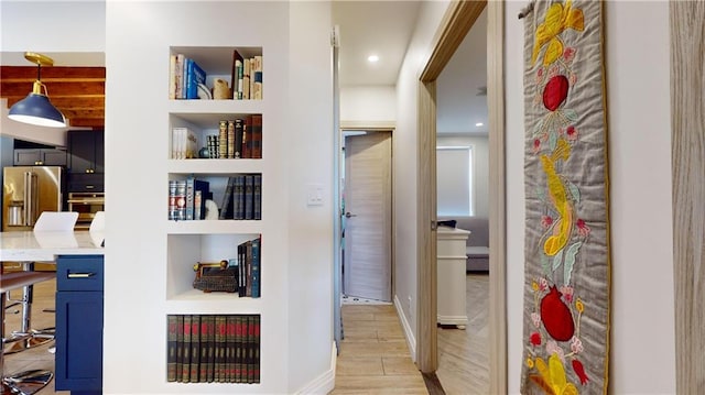 hall with beamed ceiling, built in shelves, and light wood-type flooring