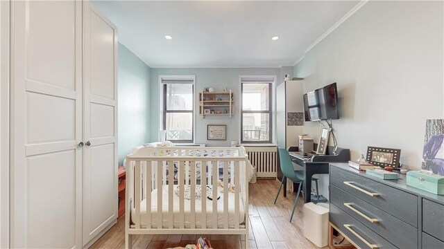 bedroom with a nursery area, radiator heating unit, crown molding, and light hardwood / wood-style flooring