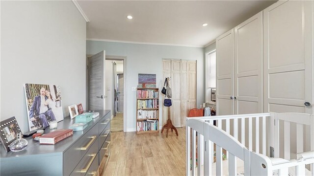 bedroom with a nursery area, ornamental molding, a closet, and light wood-type flooring