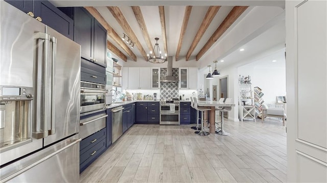 kitchen with blue cabinetry, white cabinetry, hanging light fixtures, appliances with stainless steel finishes, and beamed ceiling