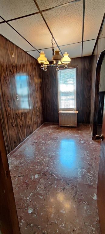 unfurnished dining area featuring a paneled ceiling, wooden walls, and an inviting chandelier