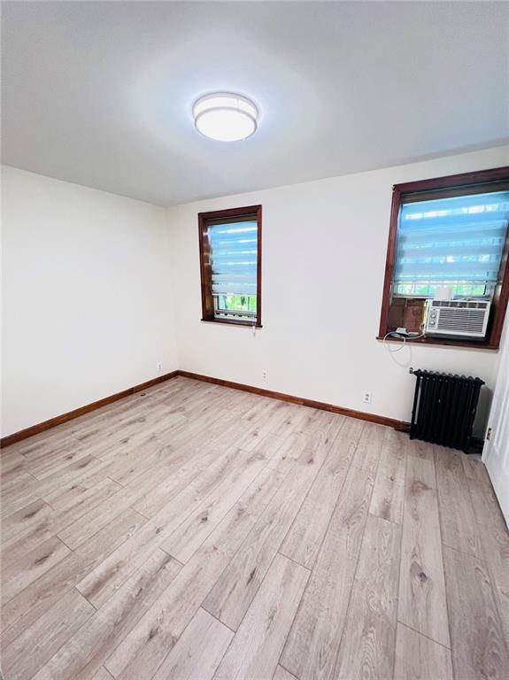 empty room featuring light hardwood / wood-style flooring, cooling unit, and radiator heating unit