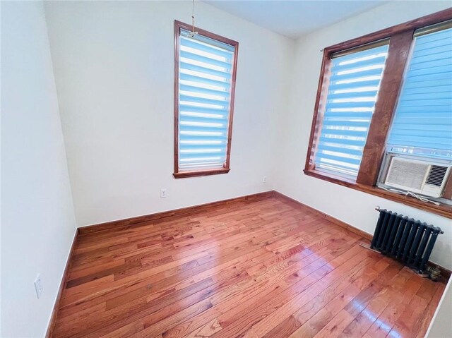 unfurnished room with a healthy amount of sunlight, radiator, cooling unit, and light hardwood / wood-style floors