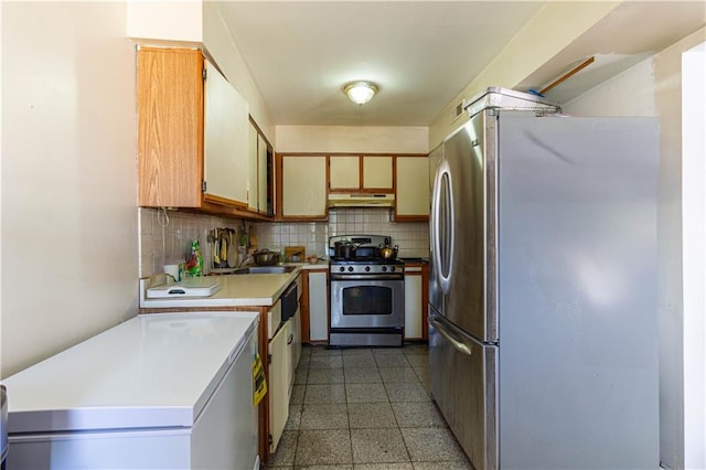 kitchen with under cabinet range hood, stainless steel appliances, backsplash, and light countertops